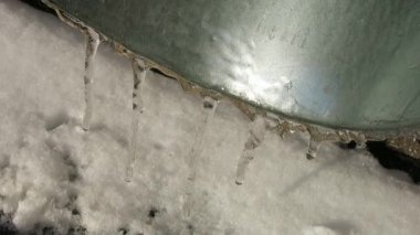 Güneşte süzülen buz saçakları olan teneke bir borunun kenarı.