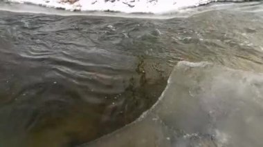 Çözülmemiş kış nehri akıntıdan akıyor, kıyıdan bir parça buz fışkırıyor.