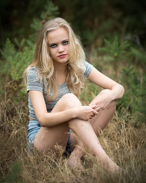 Mooie blonde tiener zittend In het gras Rechtenvrije Stockfoto's