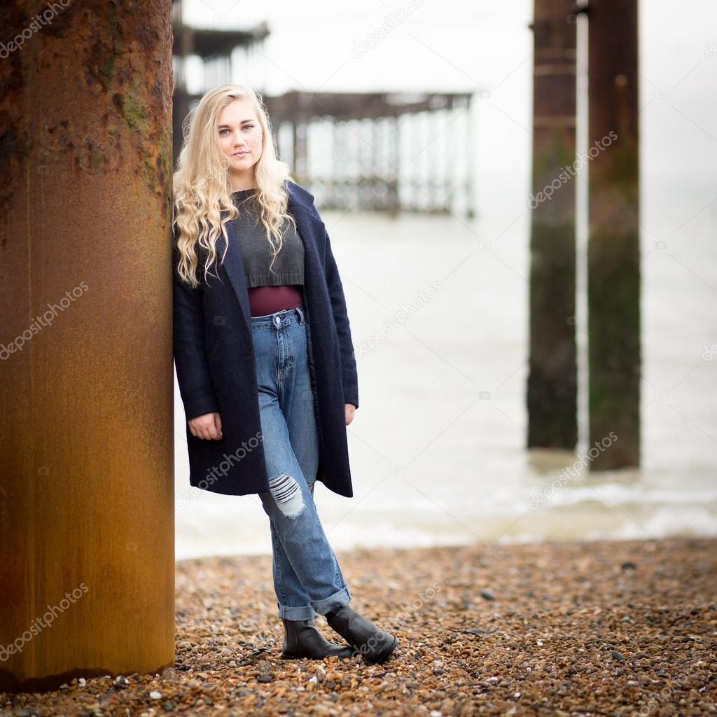 Blond Teenage Girl Leaning Against a Rusty Pier Support