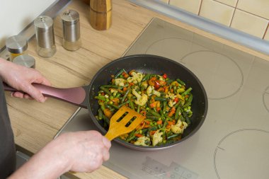 Bir kadın kızartma tavasında sebze pişiriyor.