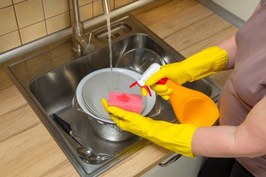 Bir kadın süngerin üzerine deterjan döker, kirli bulaşıkları lavaboda yıkar.