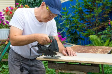 Bir adam elektrikli bir yapbozla tahtayı testereyle kesiyor..