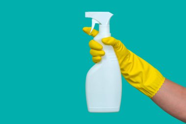 Sarı lastik eldivenli bir el mavi arka planda izole edilmiş beyaz bir sıvı sprey tutar..