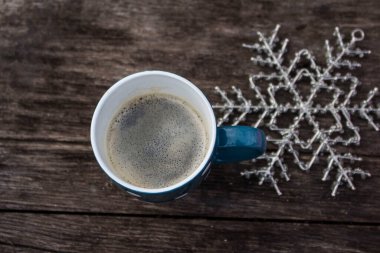 Koyu mavi kupa, taze kahve ve ahşap zeminde büyük kar tanesi süsü.