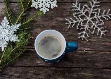 Tahta masada, köknar dalı ve kar tanesi süslemeleri olan sıcak kahve kaplı mavi kupa.
