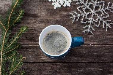 Mavi kupa, ahşap masa üzerinde kahve ve dışarıda kış süsü.