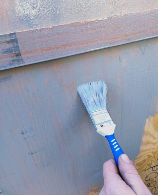 Adam ahşap bir duvarı fırçayla gri boyayla boyuyor.