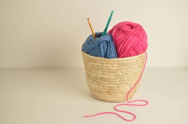 Mavi ve pembe yün toplar sepetin içinde, el işi için kancalarla.