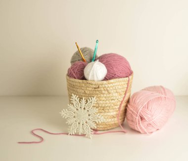 Pastel renkli yün toplar sepetin içinde beyaz kar taneli el işleri için kancalarla örgü örüyorlar.