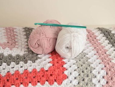 Örgü örülü yün toplar. Büyükanne kare battaniyesi sepette ve kancada.