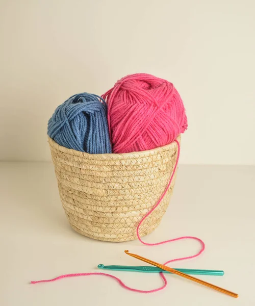 Mavi ve pembe yün toplar sepetin içinde, el işi için kancalarla.