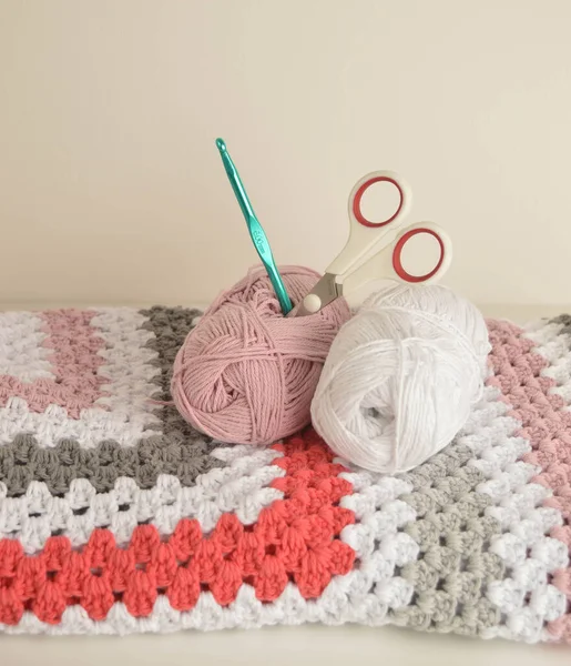 Örgü örülü yün toplar, sepetli kare battaniye, örgü kancası ve makaslı.