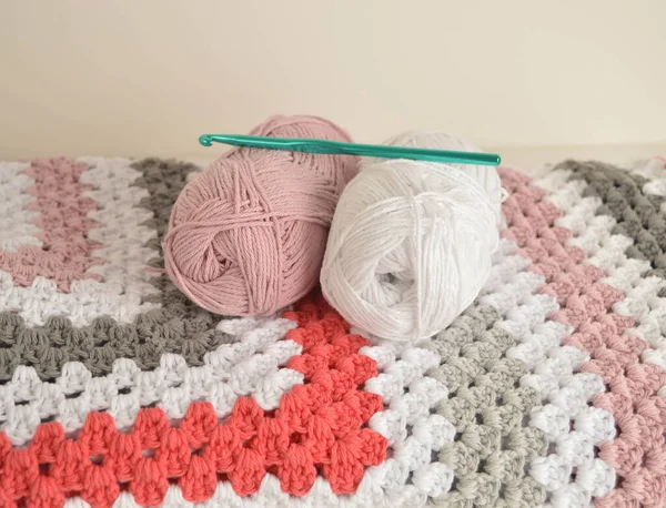 Örgü örülü yün toplar. Büyükanne kare battaniyesi sepette ve kancada.