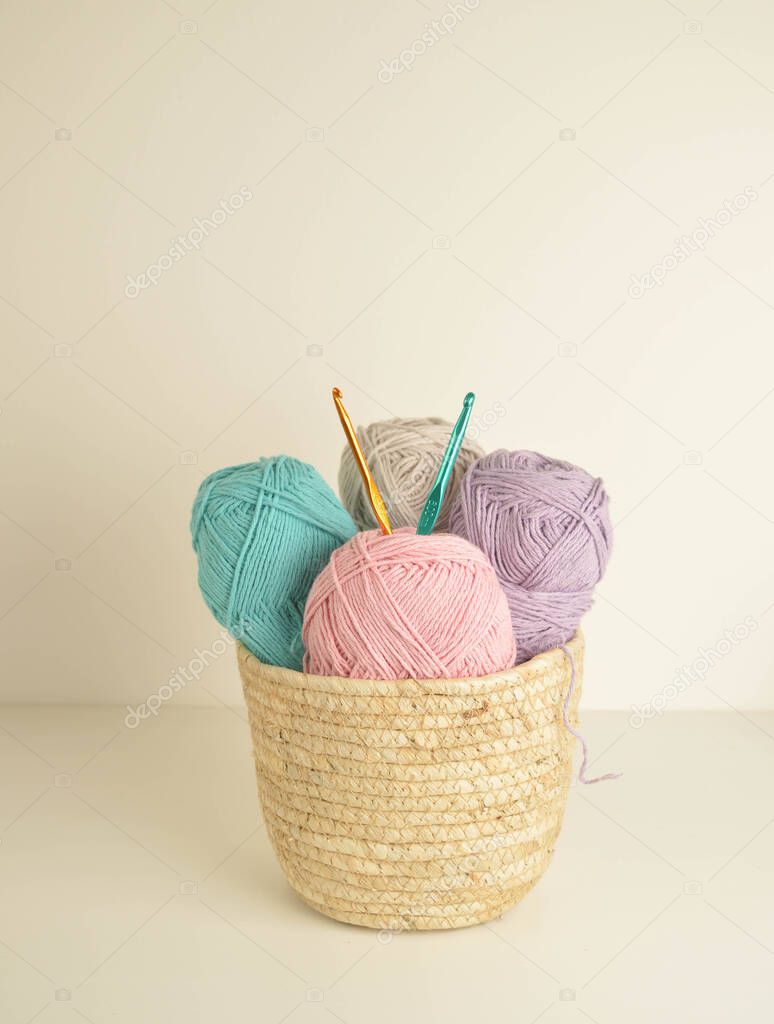 pastel colored woolen balls in basket with crochet hooks for handicrafts
