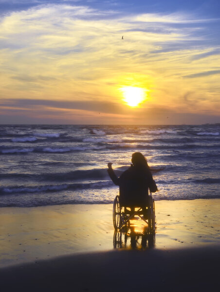 Sunset, makes sightseeing on the beach a woman on a wheelchair