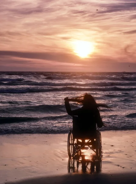 Tramonto, rende visite turistiche sulla spiaggia una donna su una sedia a rotelle Fotografia Stock