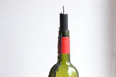 Siyah mumla süslenmiş koyu kırmızı bir şarap şişesi. Beyaz arka planda ev yapımı cam şamdan.