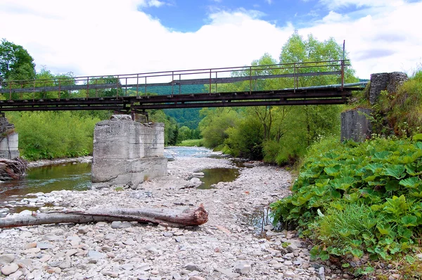 Oude ijzeren brug over de rivier op een achtergrond van beboste heuvels — Stockfoto