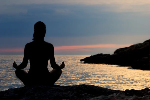 Denizin kenarında Lotus pozisyonda günbatımında meditasyon kadın silüeti. Arkadan Görünüm. Meditasyon kavramı.