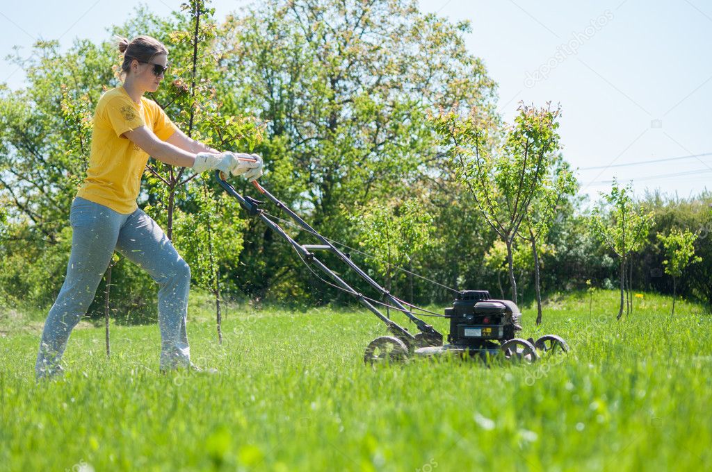 Young female in yard - pushing grass trimming lawnmower