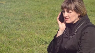 Kadın telefonda bir yeşil çayır üzerinde oturan söz