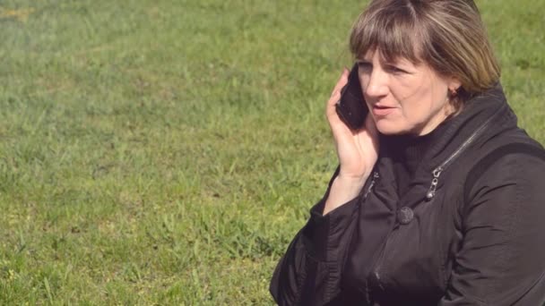 녹색 풀밭에 앉아 전화 통화 하는 여자 — 비디오