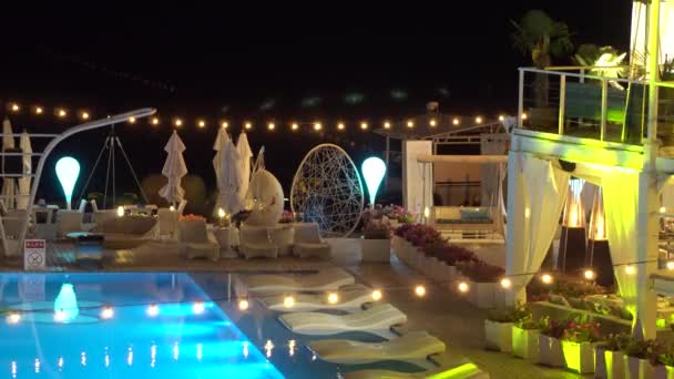 A girl sits in a chair on the shore of the pool in the evening — Stock Video