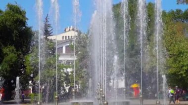 Bir çeşme ile şehir parkı. Bir bina, ağaçlar ve insanlar tiyatro görebilirsiniz