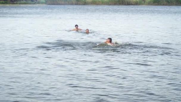 Ung man simmar i sjön. Kvinna och tonåringen tittar på honom — Stockvideo