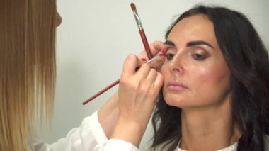Profesyonel makyöz genç bir kadına göz farı sürüyor..