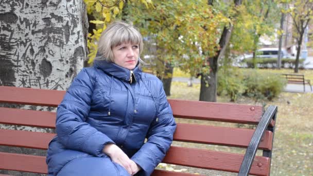 Uma jovem se senta em um banco em um parque da cidade — Vídeo de Stock