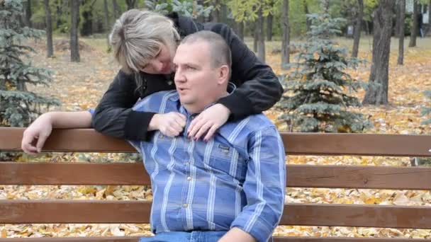 Жінка обіймає чоловіка, який сидить на лавці — стокове відео