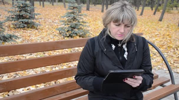 Жінка в осінньому парку, що працює з планшетом — стокове відео