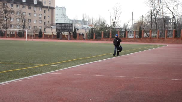 El chico con una bolsa de deporte va alrededor del terreno de juego — Vídeo de stock