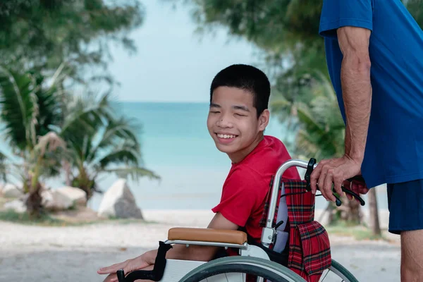 Asian special child on wheelchair is smiling, playing, doing activity on  sea beach with father,Lifestyle of disability child, Life in the education age, Happy disabled kid in travel holidays concept.