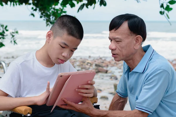 Special need child on wheelchair use a tablet with his parent,Nature background,Study or Work at home for safety from covid19,Life in new normal education of disability kid,Happy disabled boy concept.