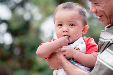 Doğada fotokopi alanı, tatlı çocuk, 7 aylık emekleme yaşı, iyi bir gülümseme ve iyi bir ruh hali olan Asyalı küçük bebek ve büyükbabanın doğadaki sevimli ifadelerinin portresi. Sağlıklı, büyük siyah gözler..