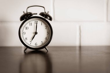 Kahverengi ahşap masa ve beyaz çimento duvar zemininde siyah klasik alarm saati, zaman kavramı..