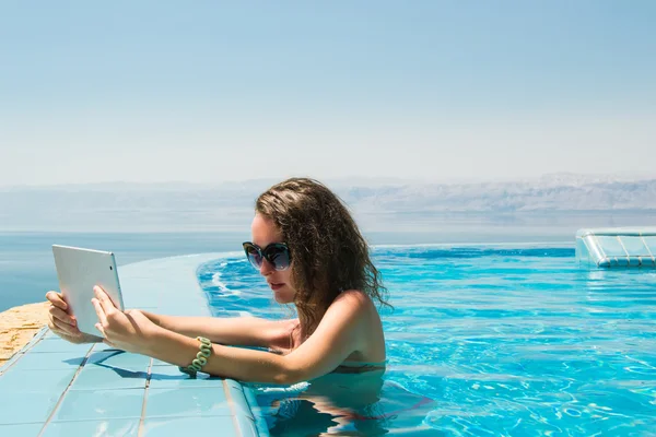 Teknoloji ve tatil kavramı. Lüks seyahat. Sonsuzluk havuzunda Resort tablet bilgisayar kullanan genç güzel kadın.