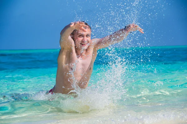 Mutlu adam tropik sahilde su, yakın çekim bir sıçrama yapar — Stok fotoğraf