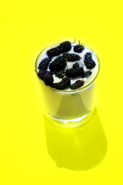 Glass of yoghurt with mulberry, yellow background, vertical — Stock Photo, Image