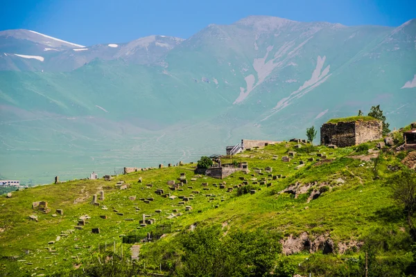 Nécropole sur pente herbeuse, montagnes de fond — Photo