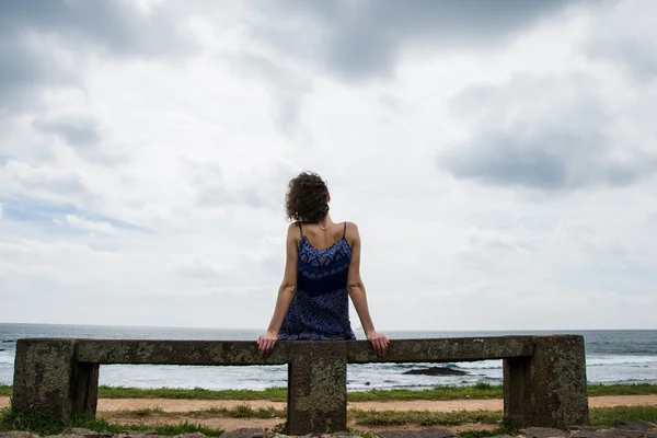 Woman sitting on stone bench near sea — Stok fotoğraf