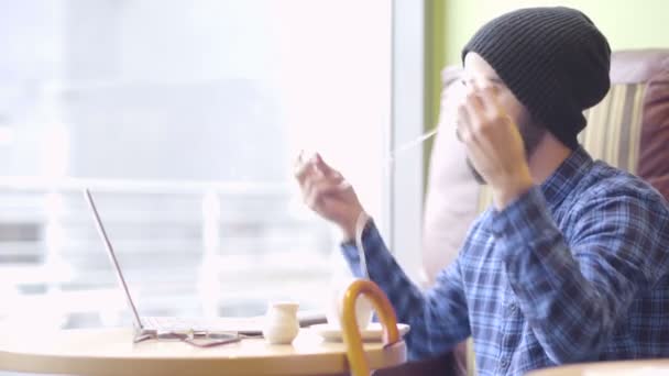 Joven hombre de moda hipster trabajando en el ordenador portátil en la cafetería — Vídeos de Stock