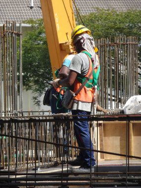 SHAH ALAM, MALAYSIA - 23 Mart 2020: İnşaat işçileri inşaat alanında çelik takviye çubuğu üretiyorlar. Kereste kalıplarını kullanarak kaplamadan önce ince telleri kullanarak birbirlerine bağladılar..