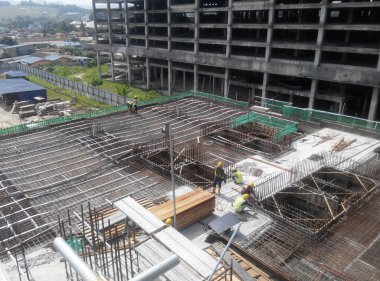 SHAH ALAM, MALAYSIA - 23 Mart 2020: İnşaat işçileri inşaat alanında çelik takviye çubuğu üretiyorlar. Kereste kalıplarını kullanarak kaplamadan önce ince telleri kullanarak birbirlerine bağladılar..