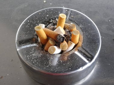Used cigarette butt in dirty stainless steel ashtray.  