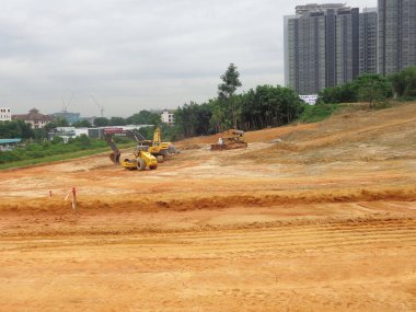 CYBERJAYA, MALAYSIA - 10 HAZİRAN 2020: Yeni gelişim alanı için toprak çalışmaları. Yokuş, ağır makinelerle budanmış. Arazi mühendisi gerekli platform seviyesini saptamaya yardım ediyor. Dünyayı kesmek ya da doldurmak için kullanılan makineler. 