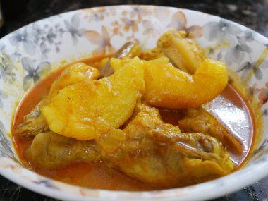 Geleneksel Malezya usulü körili tavuk, beyaz çiçekli bir tabakta servis edilir. Yemek soslu ve büyük doğranmış patatesle kaplı.. 